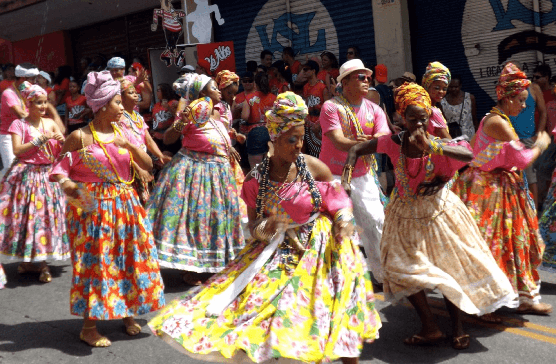 MRegistro de um grupo de mulheres dançando com trajes típicos durante o carnaval de rua.